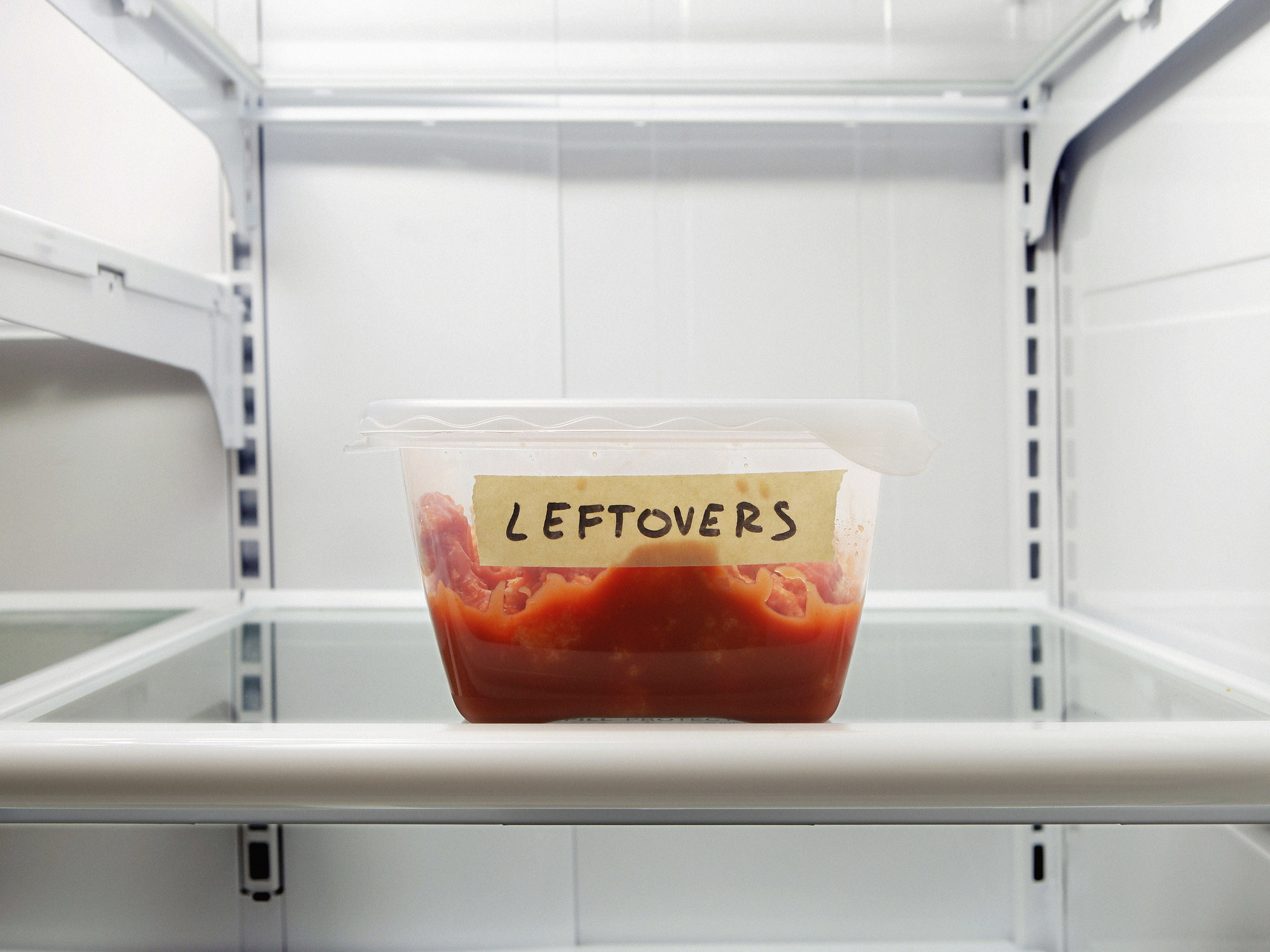 A container of leftovers on an otherwise empty fridge shelf