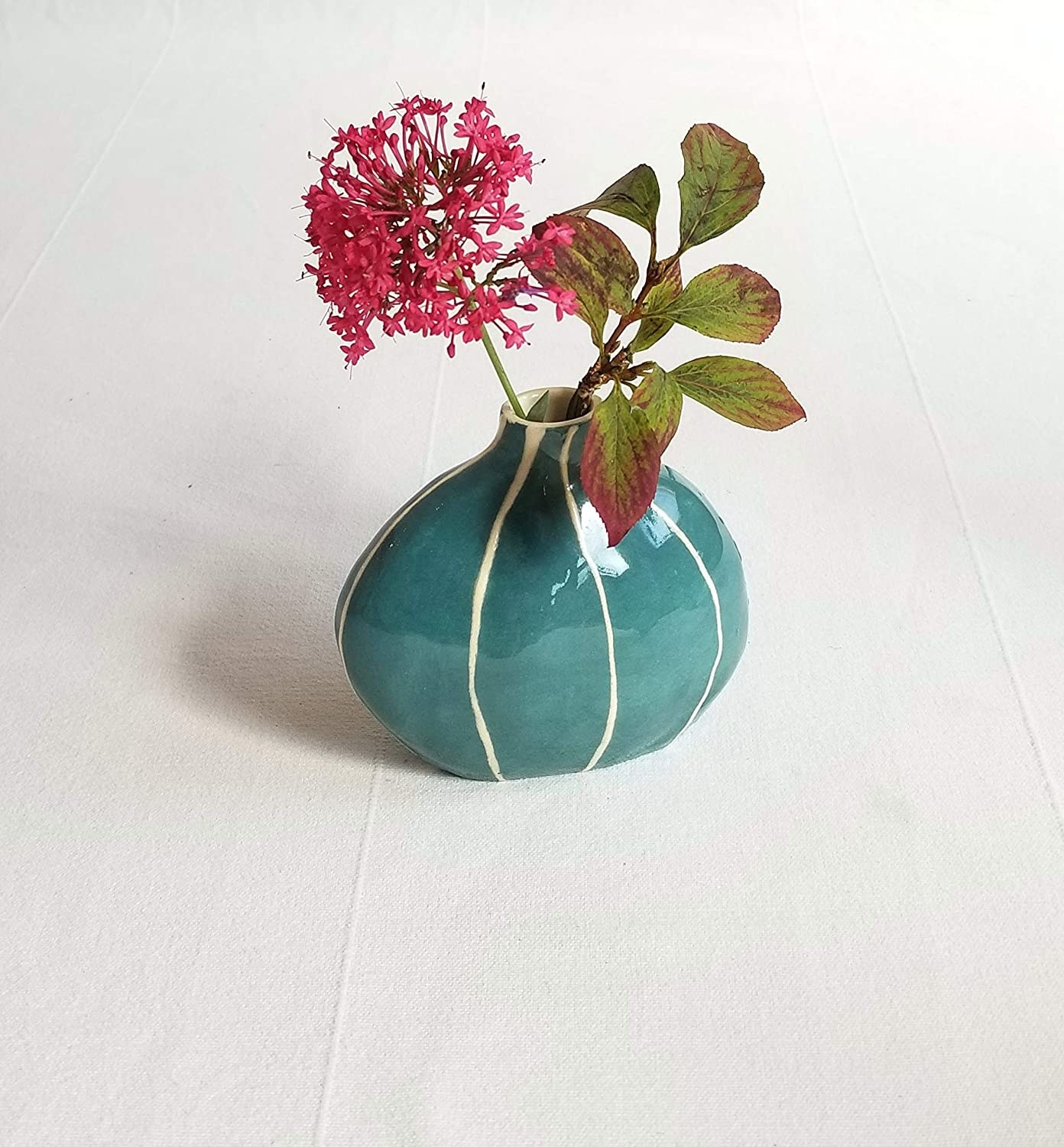 a teal blue vase with white stripes and a flower bud inside of it 