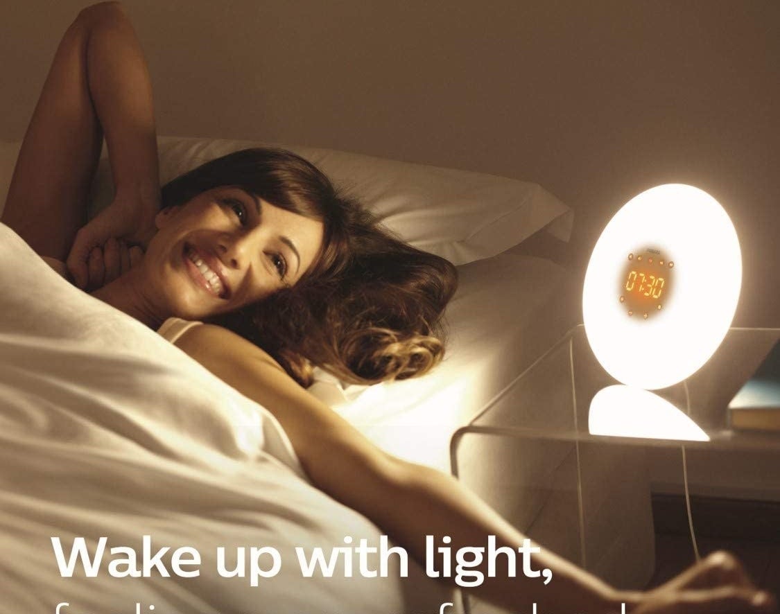 A person laying down and smiling with the light on their bedside table.