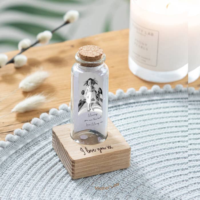 a tiny glass bottle with a photo of a child and parents inside and a note on top of a wooden stand that says &quot;i love you&quot;