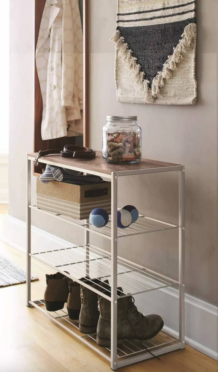 The four-tier shoe rack with a rustic oak finish holding shoes and dog toys and treats