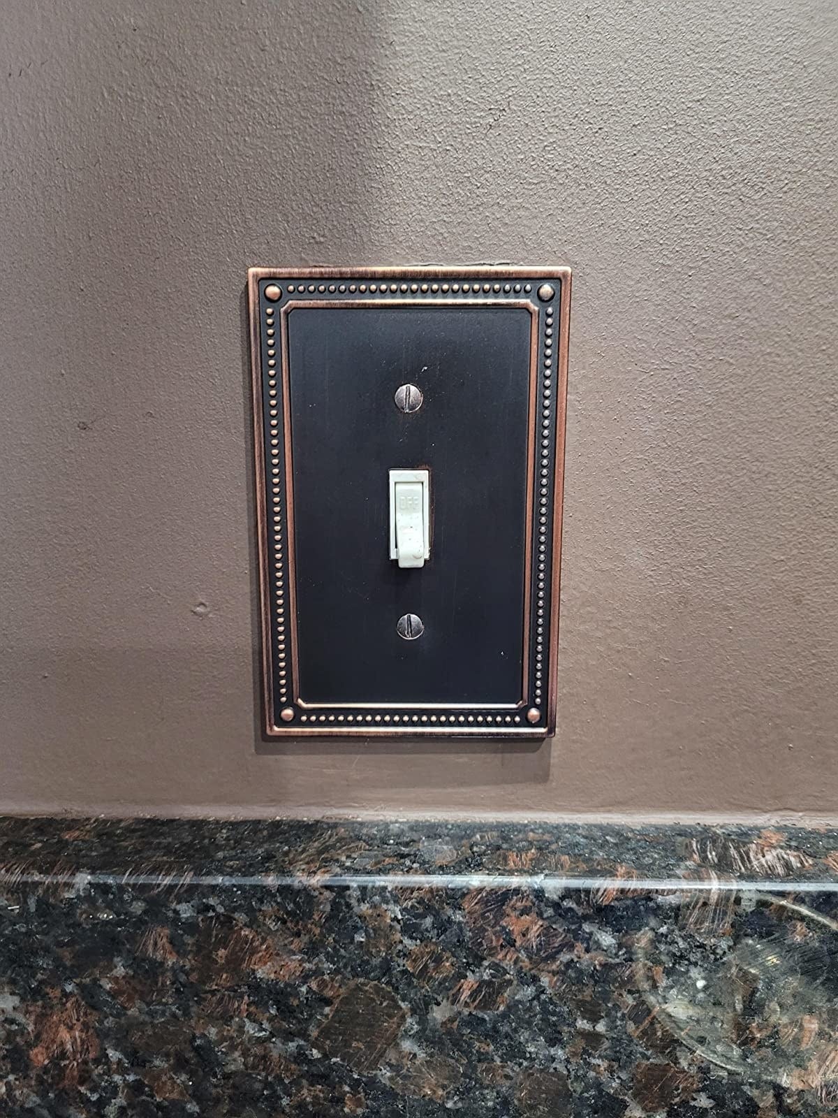 reviewer image of the bronze and copper single switch Franklin Brass Classic Beaded Single Switch Plate Cover over a light switch