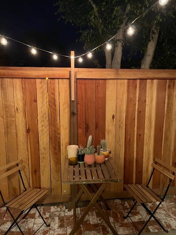 same string lights above a patio table and chair set covered with plants