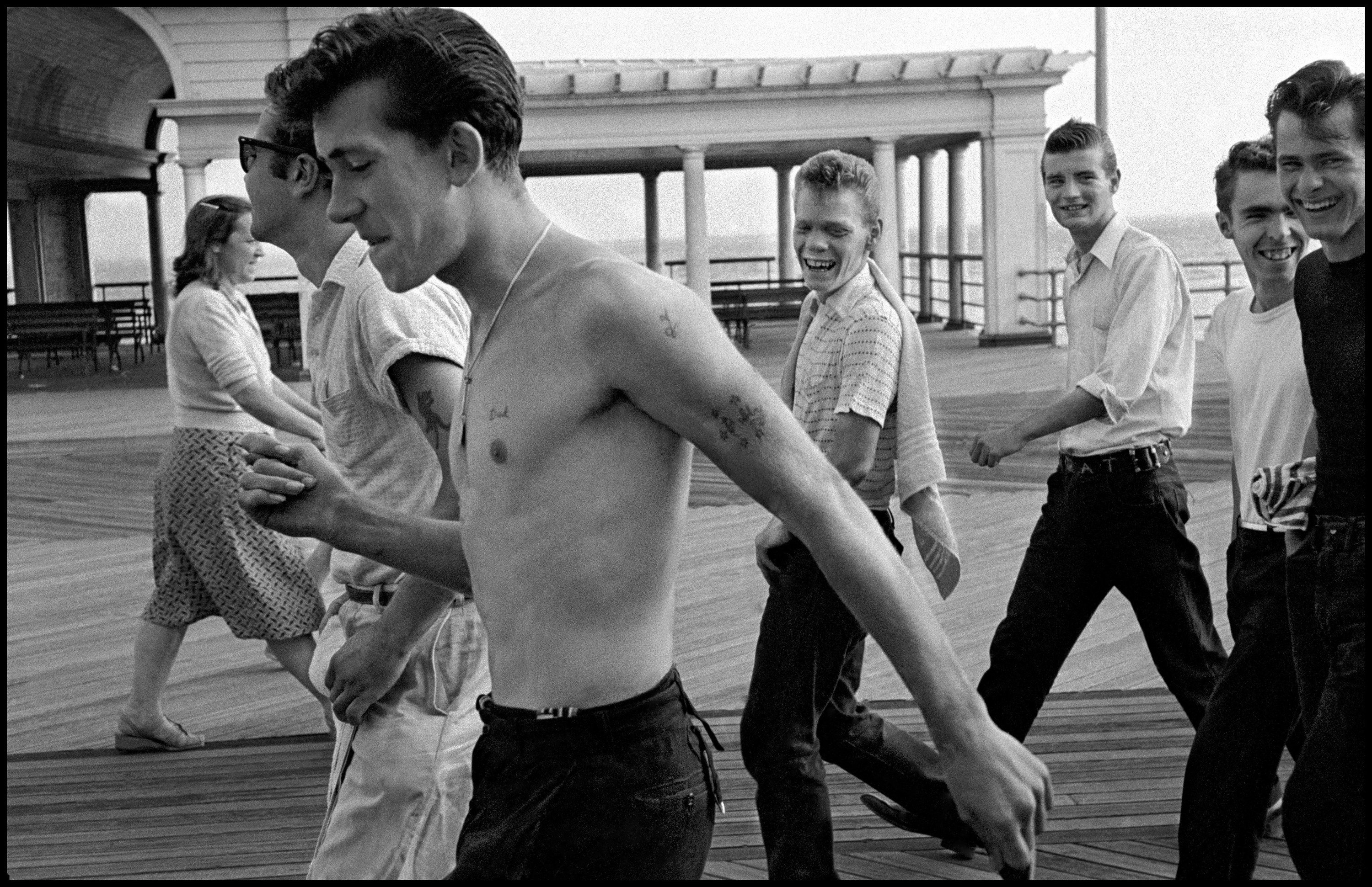 A gang of friends, one with his shirt off and all with ducktail hairdos, on the Coney Island boardwalk in the 1950s