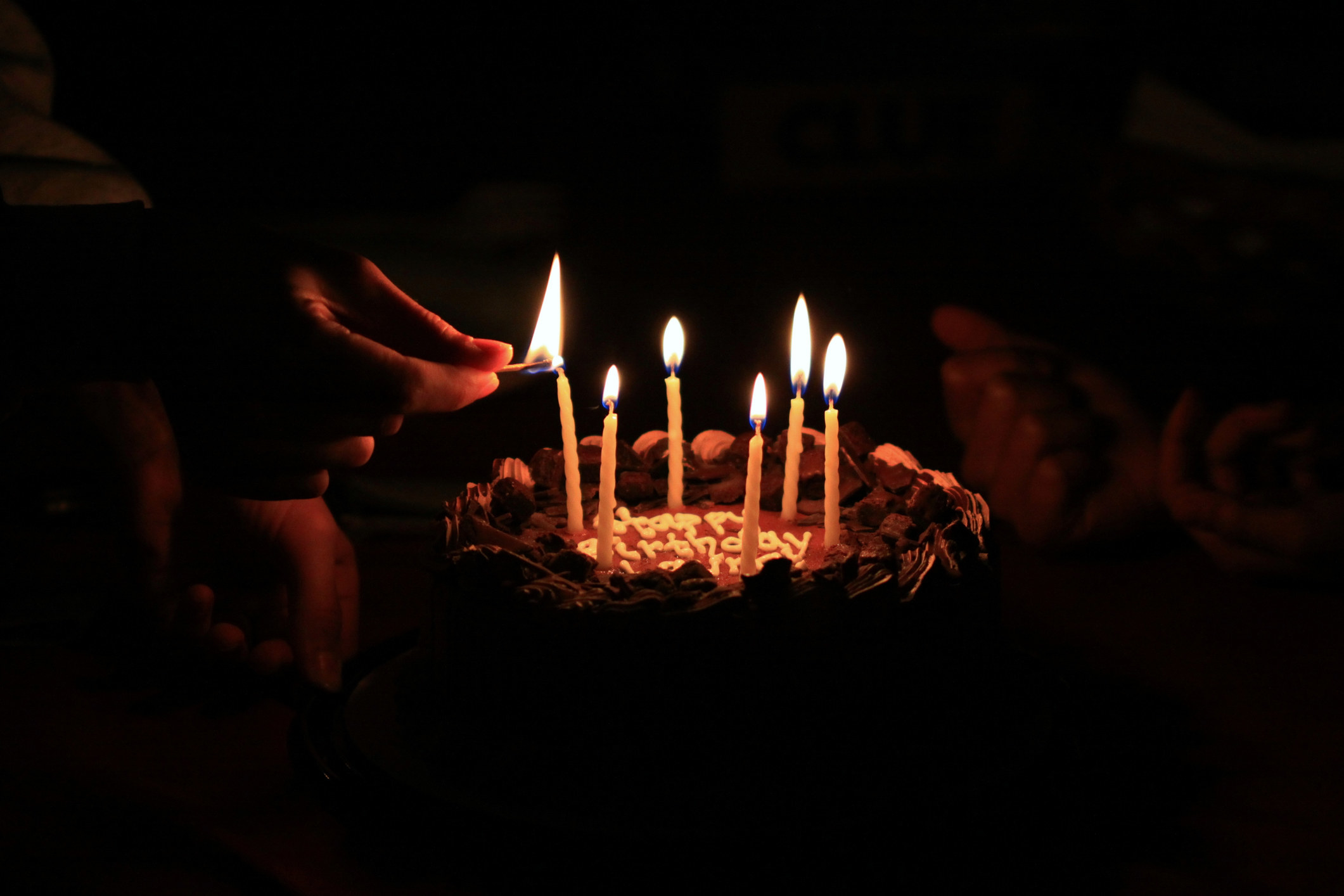 hands lighting a birthday cake