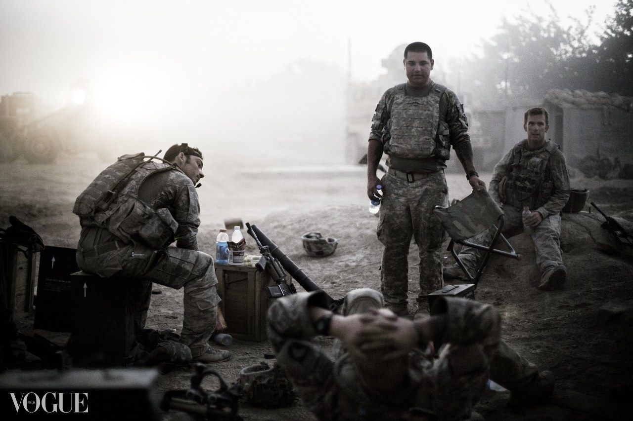 Four soldiers in a war zone relaxing and talking, with one standing and three seated