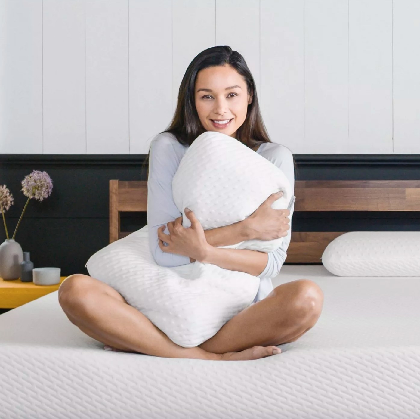 The Tuft and Needle memory foam pillow being held by a model sitting on a bed