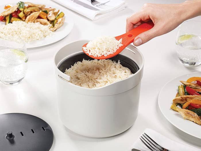 The cooker with rice inside being scooped out with the paddle