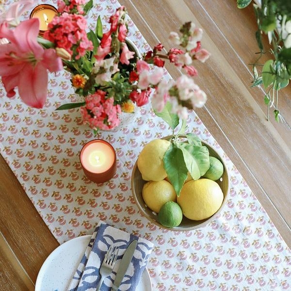 the table runner with a pink floral pattern on a wooden table covered with candles and a lemon bowl