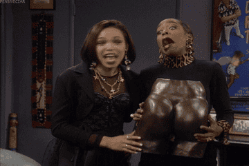 Gina and Pam making an &quot;I gotcha!&quot; face while holding a statue of a butt