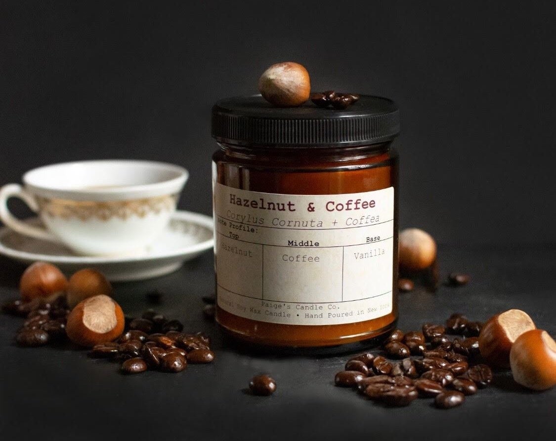 the amber-colored glass candle with black lid and the words &quot;hazelnut &amp;amp; coffee&quot; on the tan label