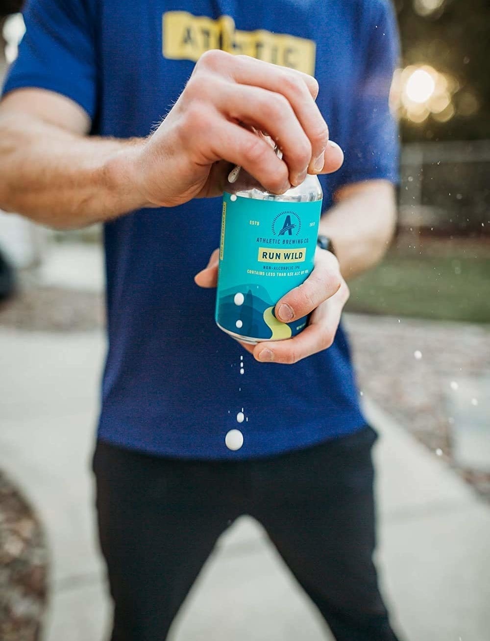 close up of a model opening a can of athletic brewing company&#x27;s non-alcoholic IPA and suds spilling out