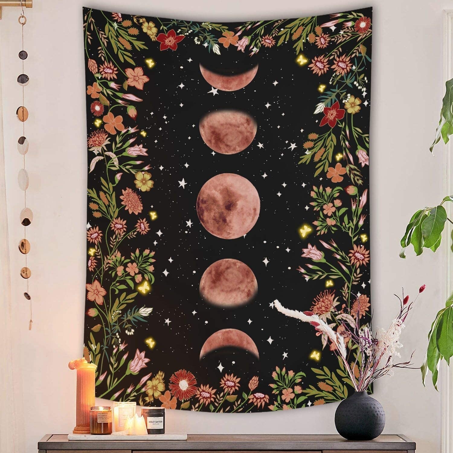 vertical tapestry hung on a wall with a black background, moon phases and stars, and flowers for a border