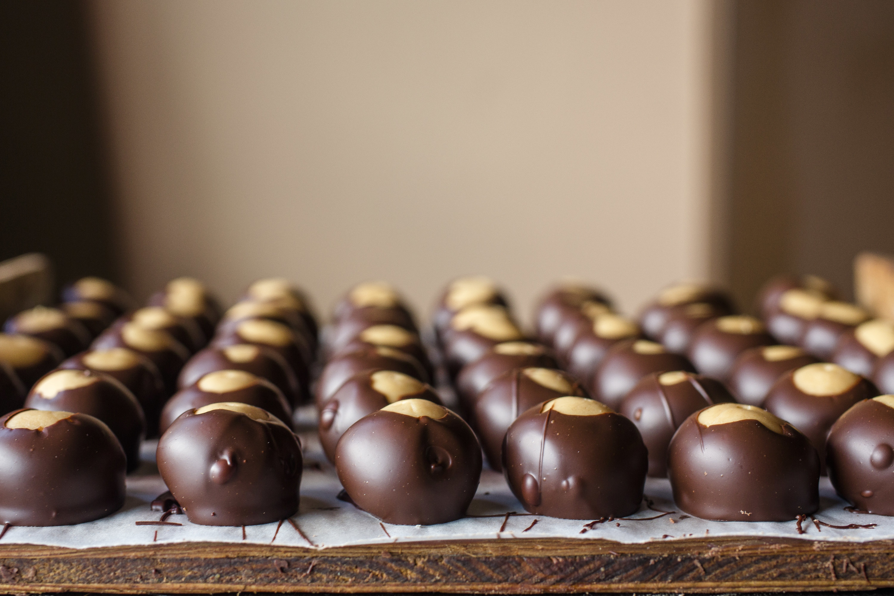 Six rows of buckeyes, chocolate-covered peanut butter candies, cooling off on parchment paper
