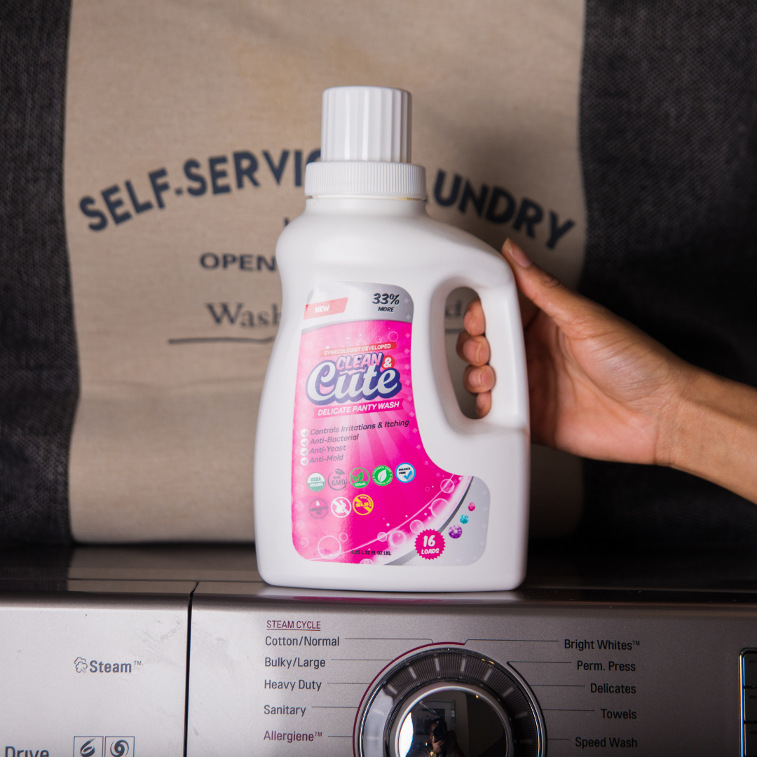 a model&#x27;s hand holds a bottle of clean and cute above a washing machine