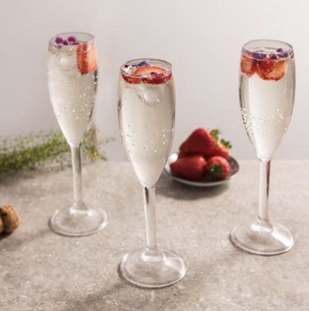 Three glasses of champagne rest on table, topped with slices of strawberries