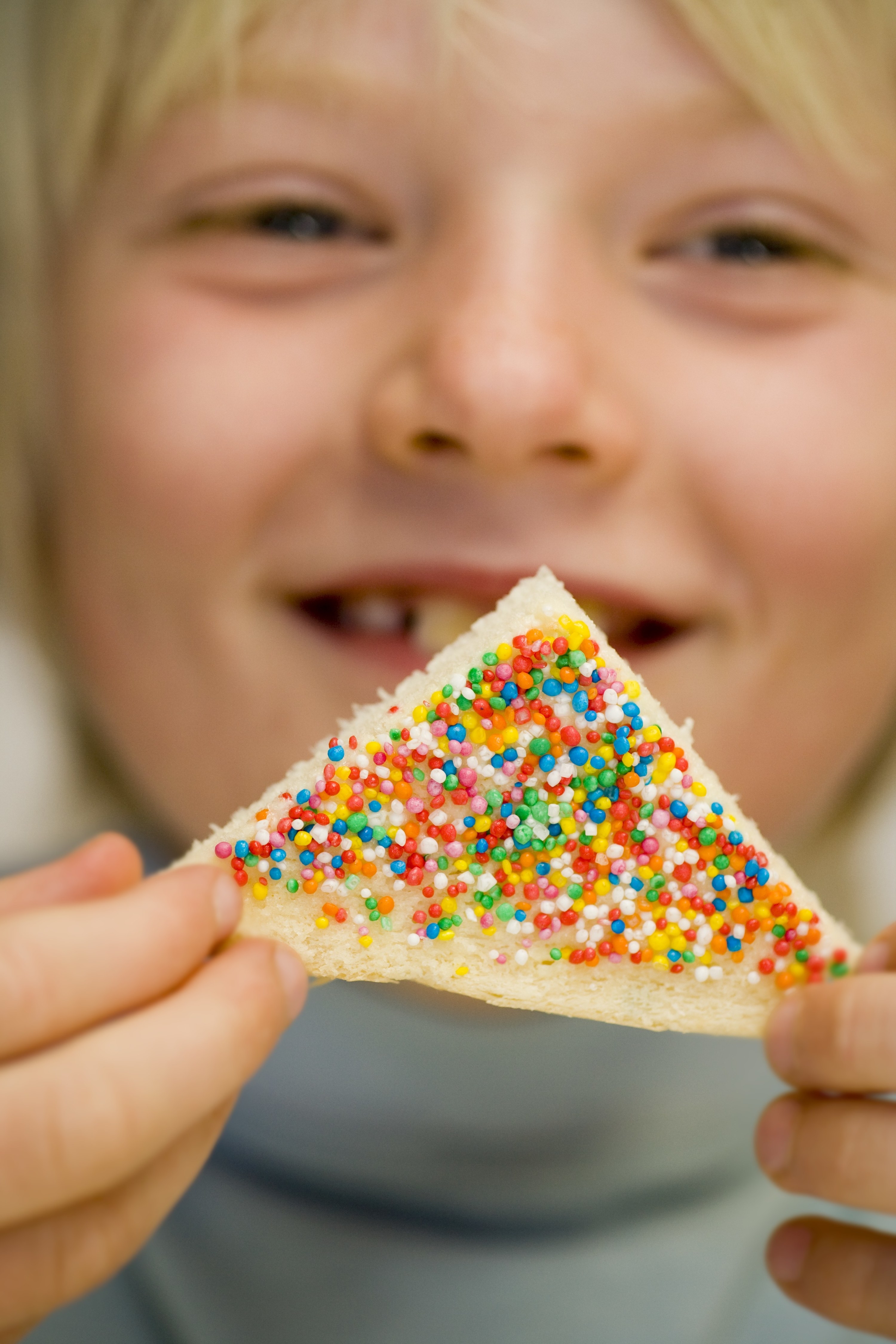 Boy smiling while holding a slice of fairy bread cut into a triangle, buttered, and topped with colorful sprinkles