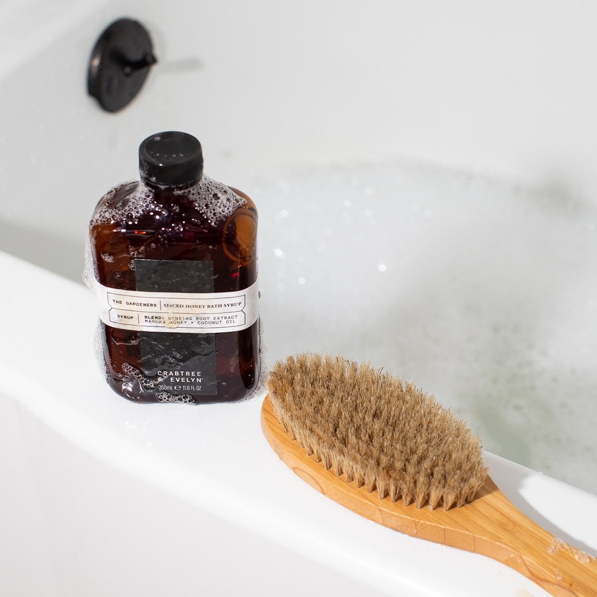 a amber bottle of bath syrup on the edge of a bathtub