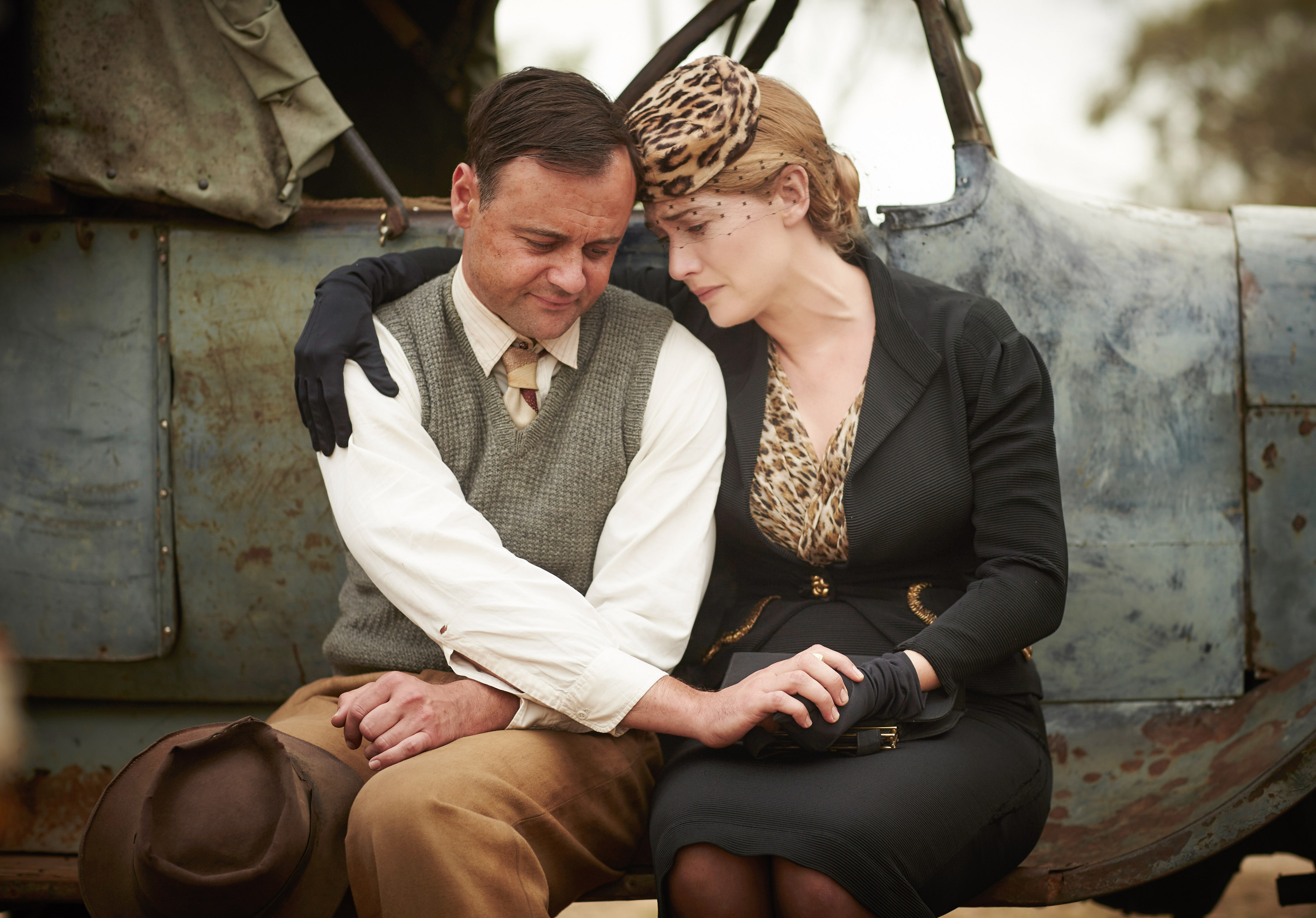 Kate wearing a leopard-print hat and long black gloves and embracing a man