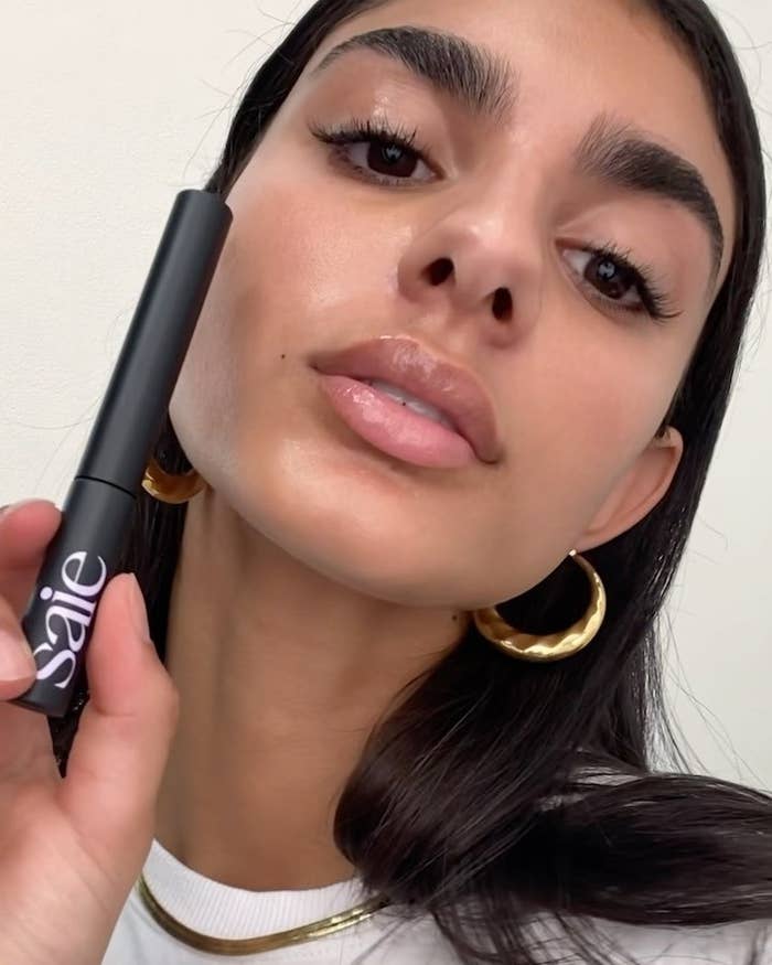 A person with full-looking brows holding a tube of brow gel