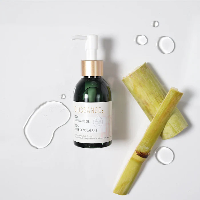 A bottle of face oil next to chopped sugar cane