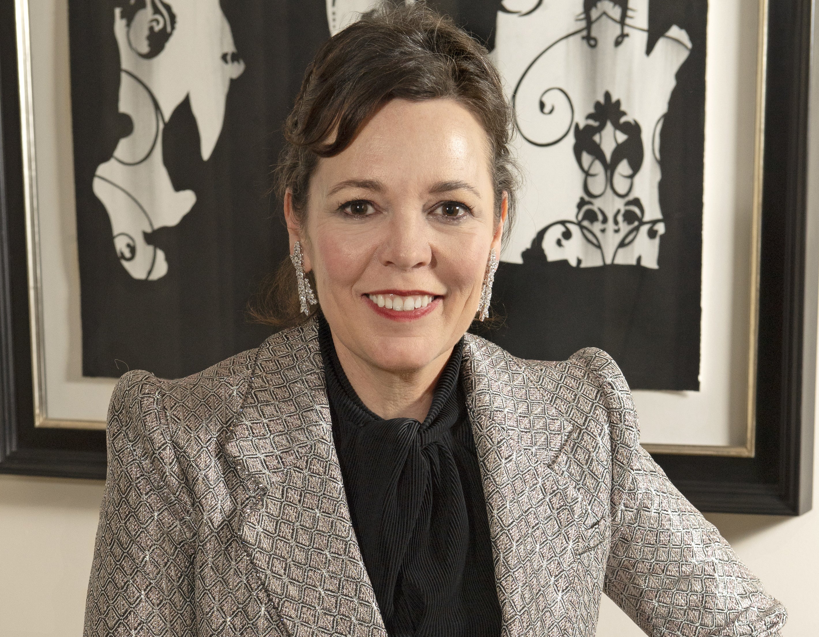 Olivia Colman smiles while sitting in a living room 