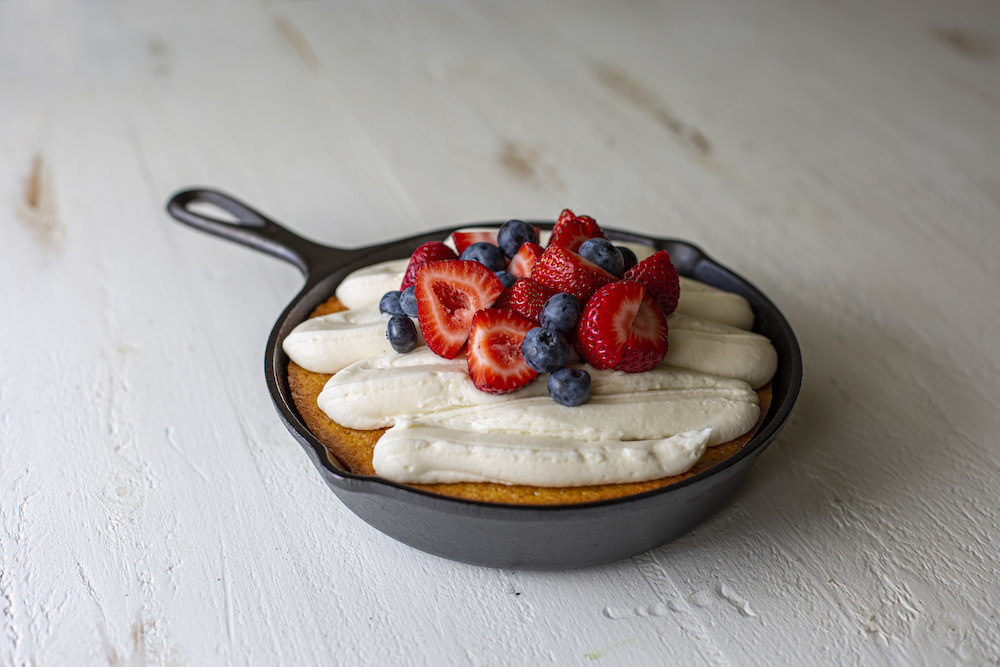cast iron skillet with a cake and fresh berries on top, on a table 