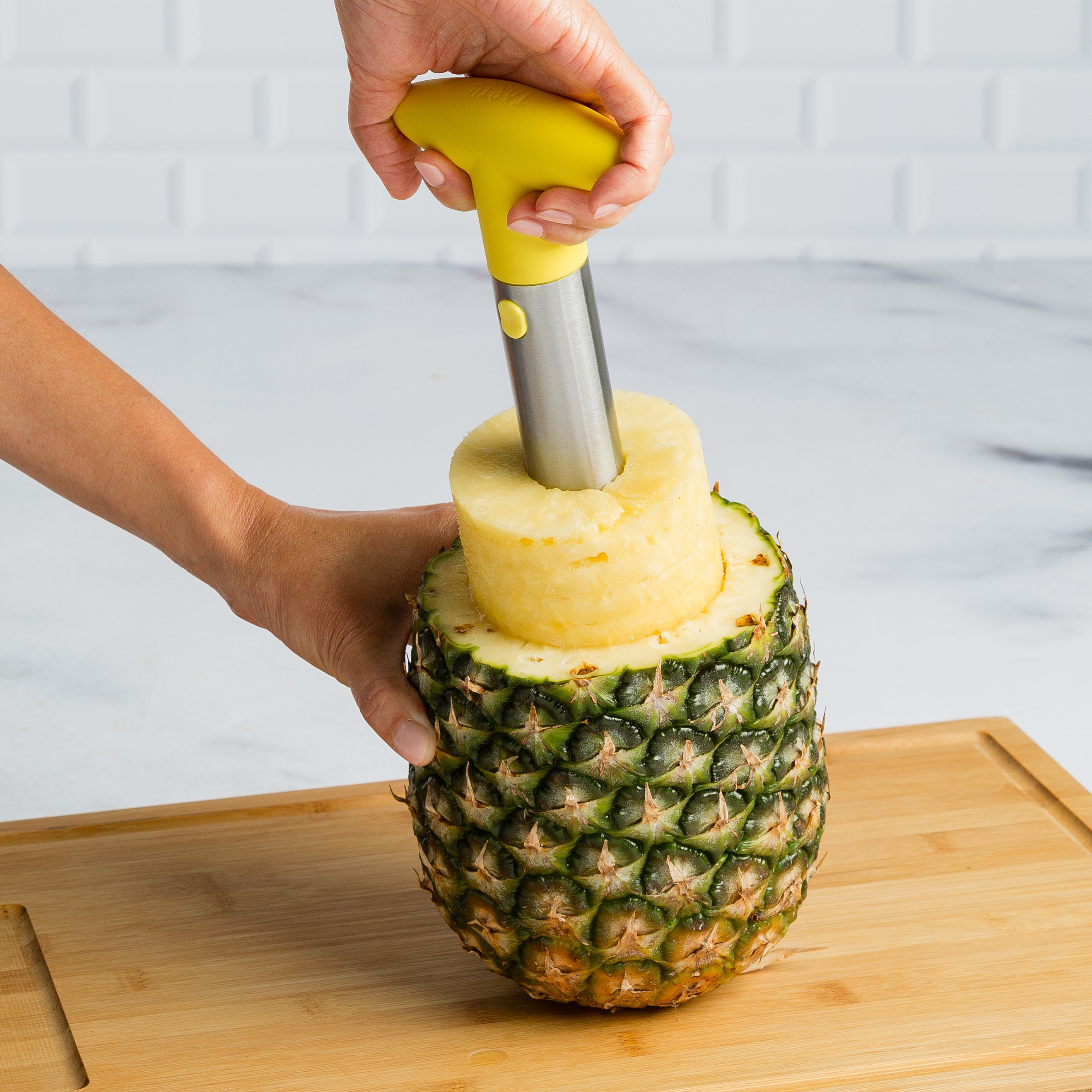 Model holding a pineapple corer and removing the inside of a pineapple