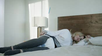 Model sleeping on their side with a white slope contoured pillow between their knees 