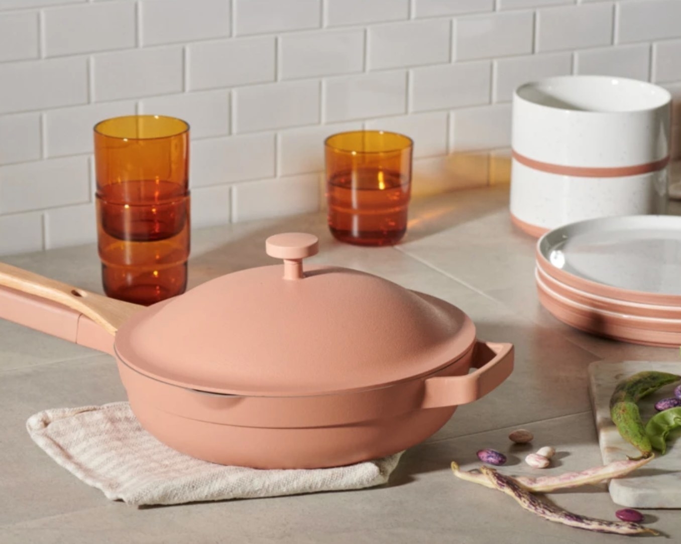 The deep skillet-like pan in a pinkish color with a full matching lid, and a bamboo stirrer attached to the handle