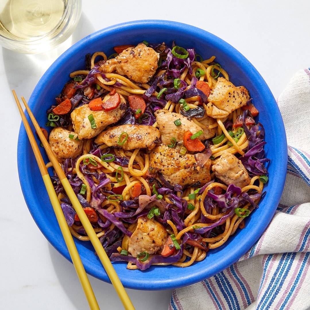 a bowl of chicken stir fry with carrots, cabbage, and noodles