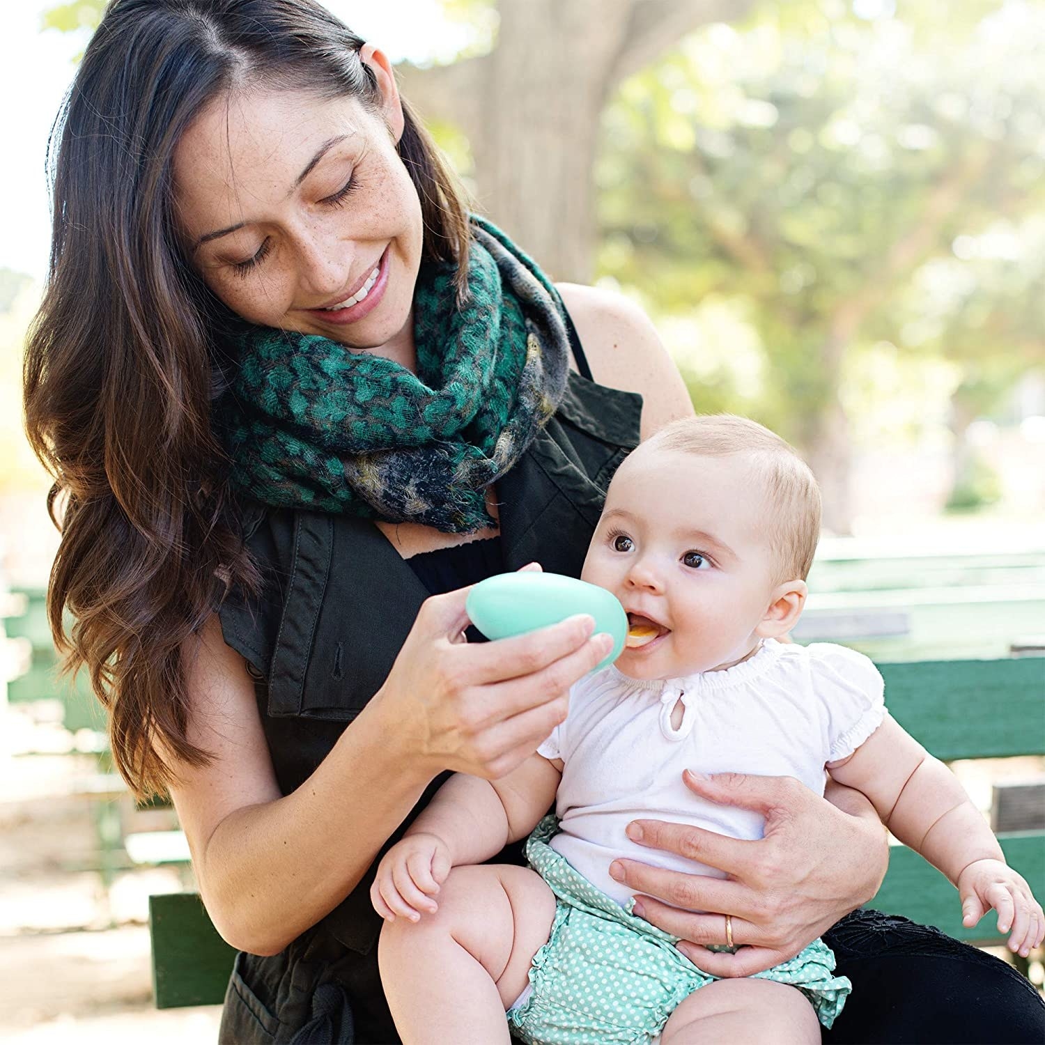 Parent feeding an infant on a park bench with the food storage spoon 