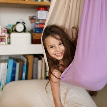 Child smiling while curled up inside the hanging fabric chair