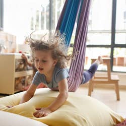Another child model swinging on their stomach, as if flying, onto a pile of pillows