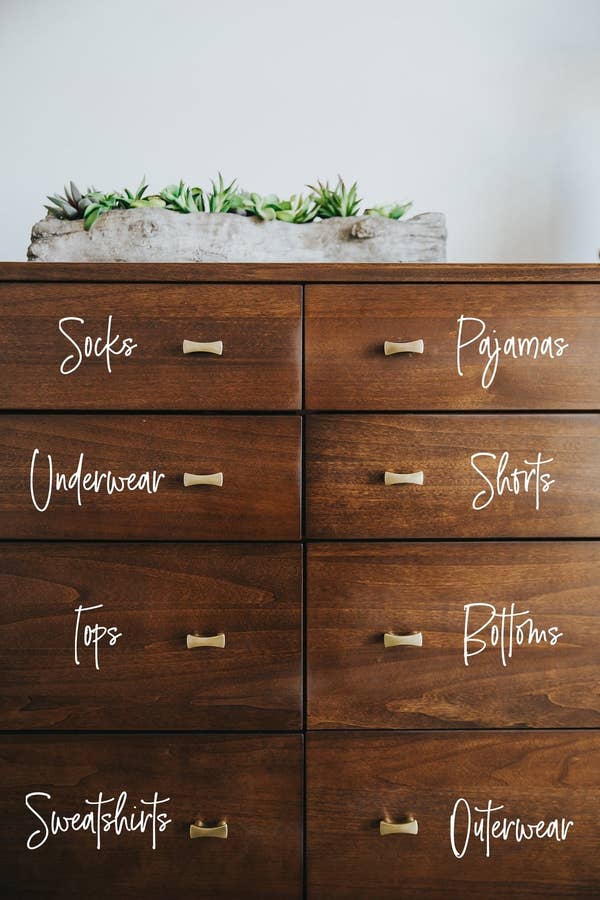 Dresser with written stickers on each drawer that say &quot;sweatshirts&quot; &quot;tops&quot; &quot;outerwear&quot; and more 