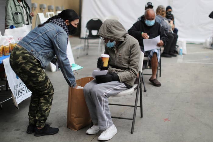 A woman in a hoodie sits on a metal chair outdoors and holds a cup of coffee after getting a COVID vaccine at a Los Angles shelter for people experiencing homelessness.