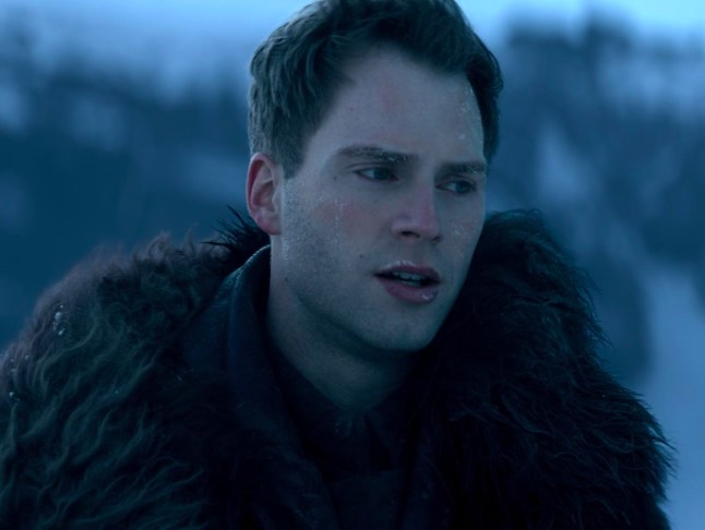 Matthias wears a fur-trimmed outfit and stands outside in a snowy area; he has a reddened face covered in frost