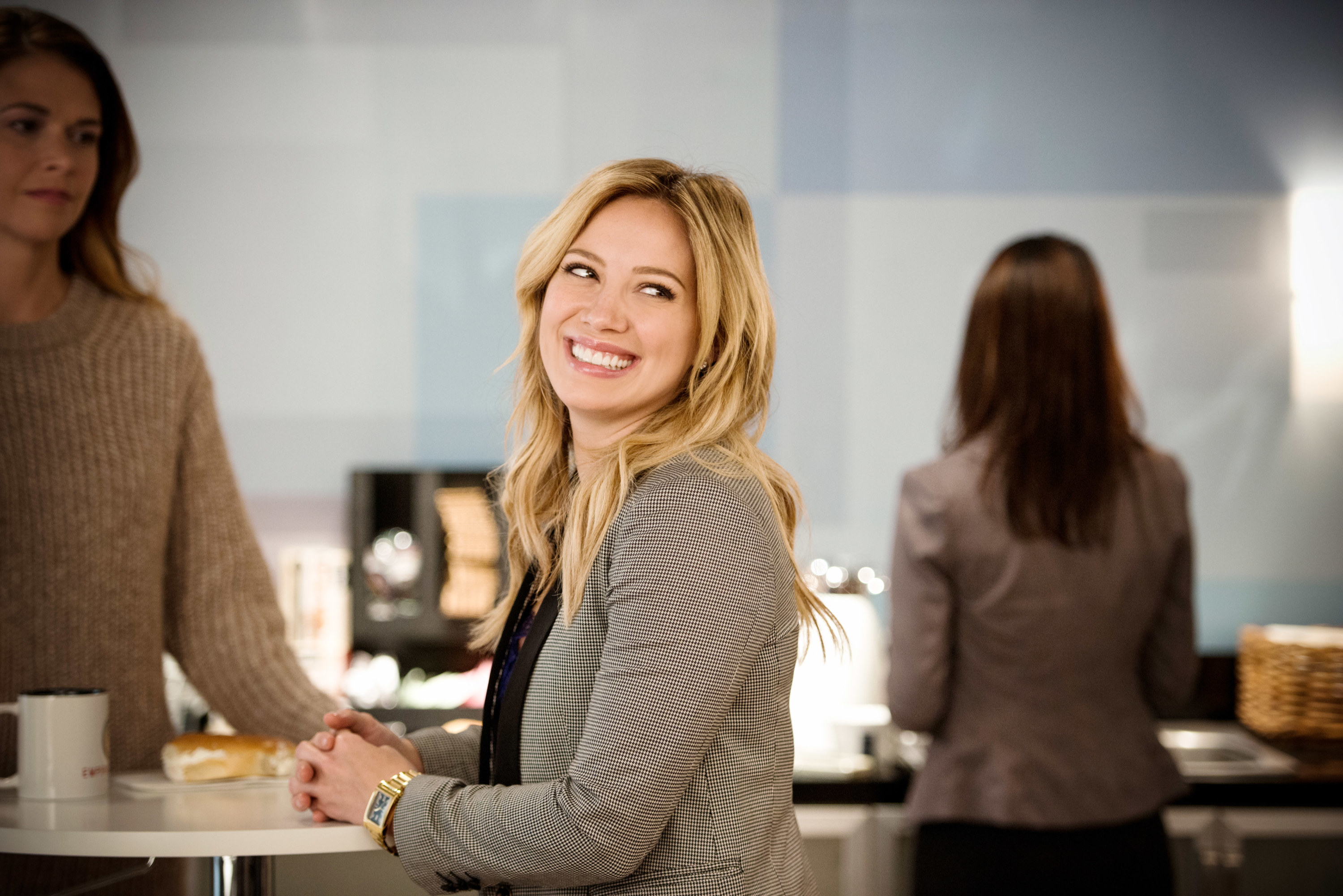 Hilary sits at a countertop and smiles over her shoulder in Younger