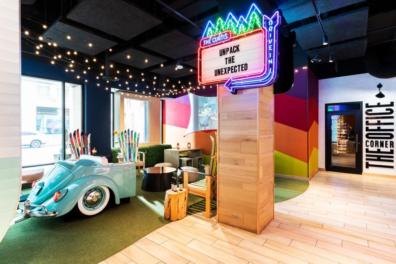 A hotel lobby with a sign that says &quot;Unpack the unexpected,&quot; an armchair made from an old car, fairy lights, and colorful walls