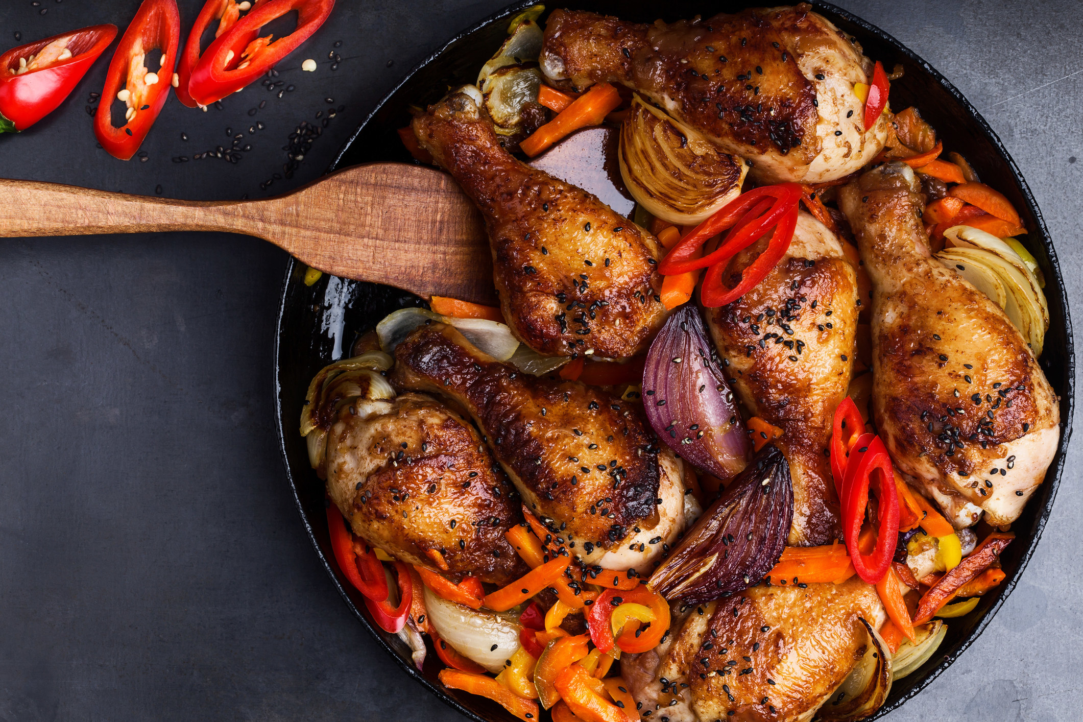 Chicken drumsticks with peppers and garlic in a cast-iron skillet.