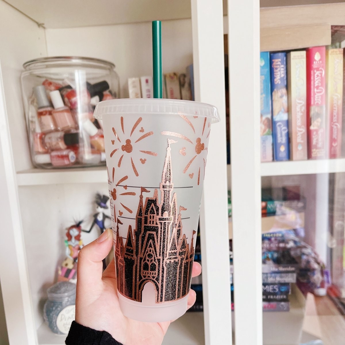 hand holding a reusable Starbucks style cup with a straw that has a sparkly Cinderella castle painted on it