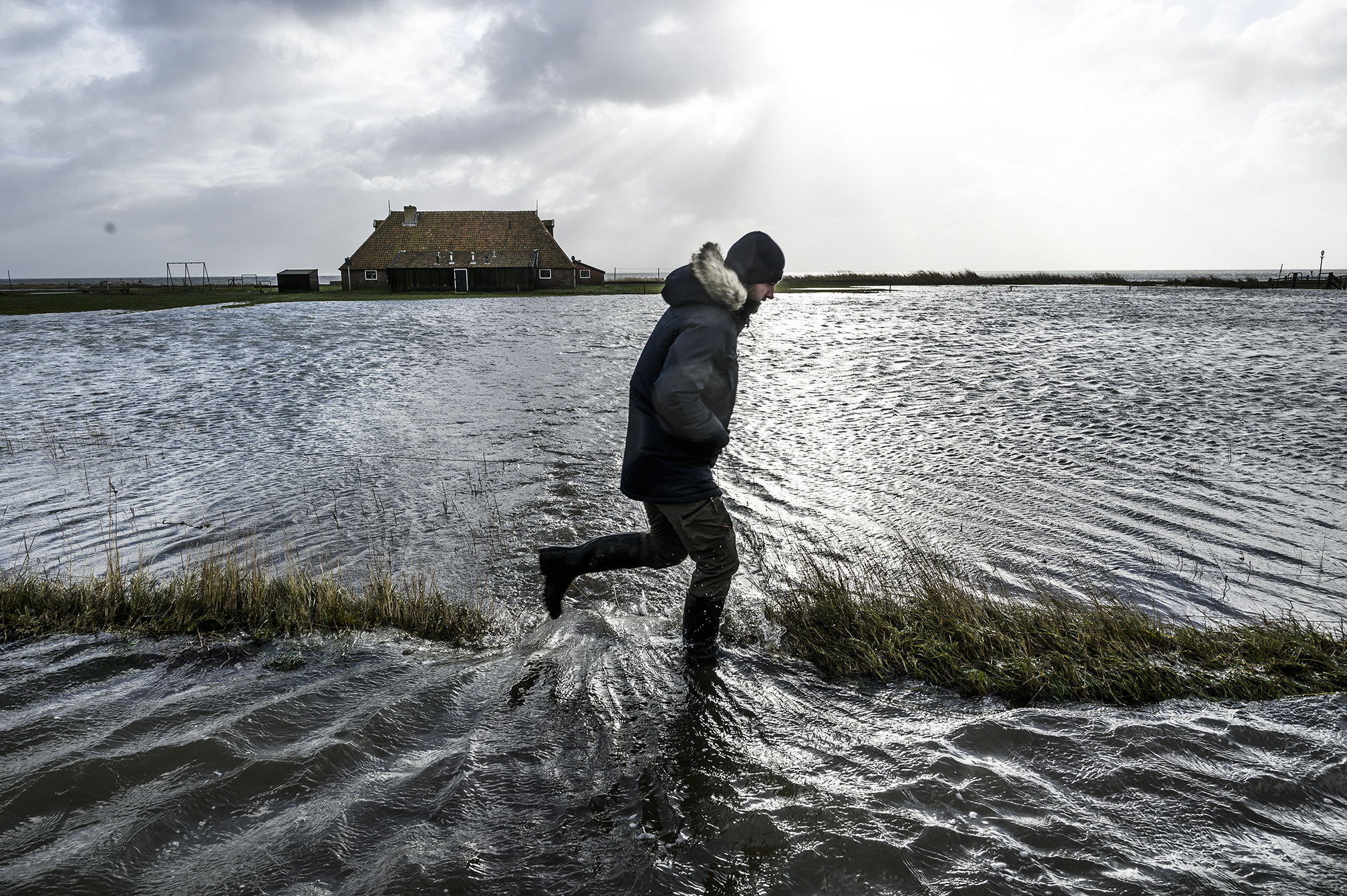 A person walking in deep water with a house off in the distance