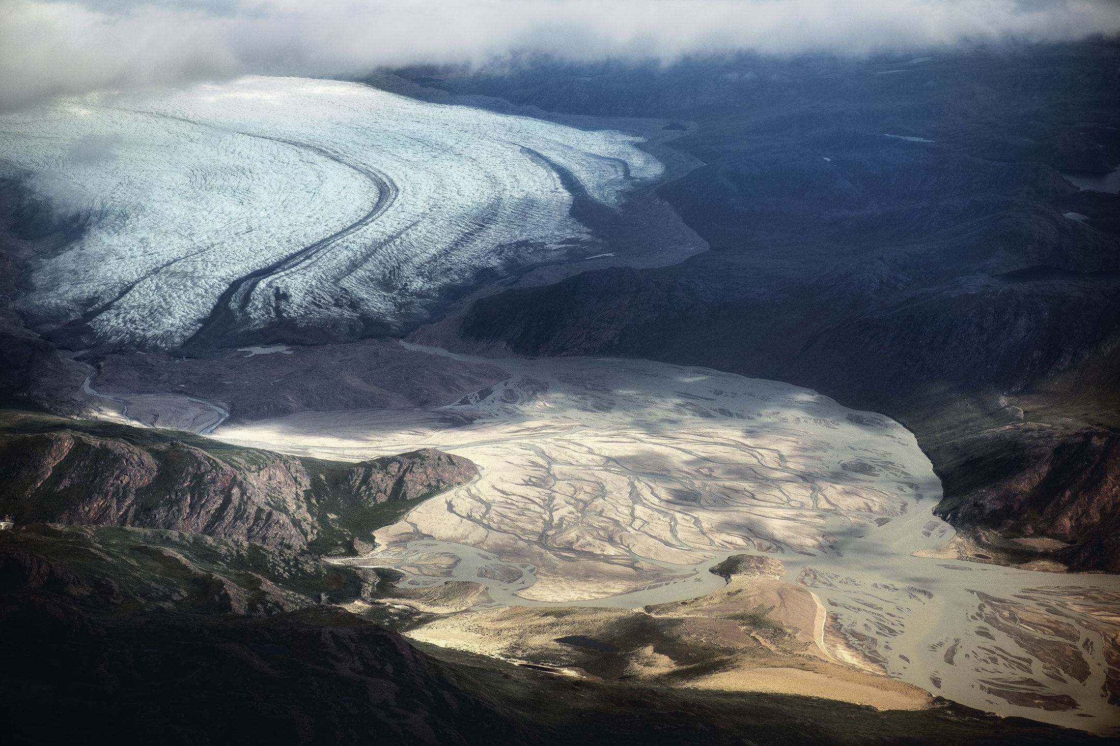 An aerial photo of a large glacier surrounded by mountains that gradually becomes a sandy series of rivers