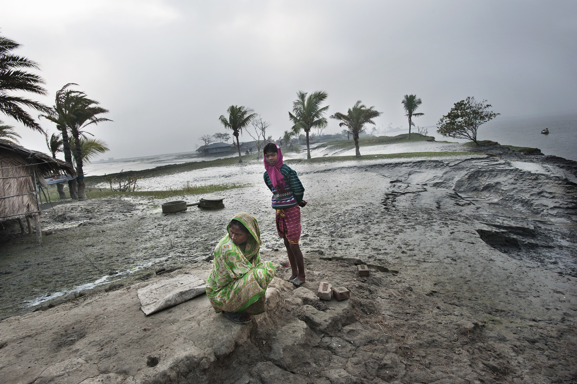 A mother and daughter on a windswept and muddy shoreline