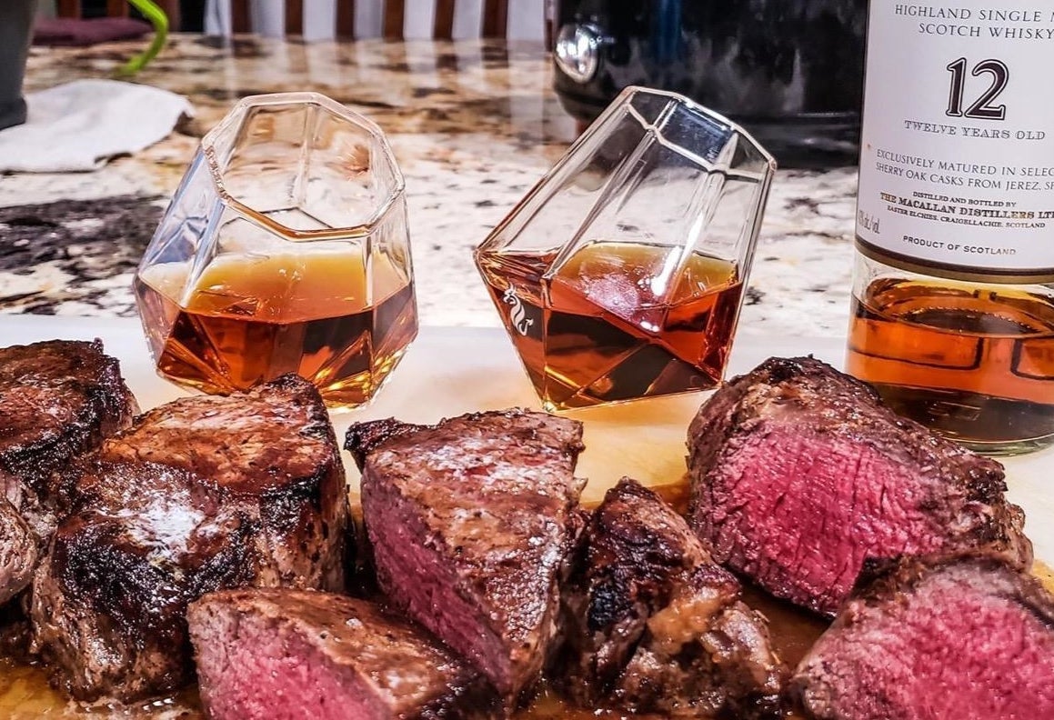 Reviewer image of the filled glasses beside a bottle of whiskey and some steak