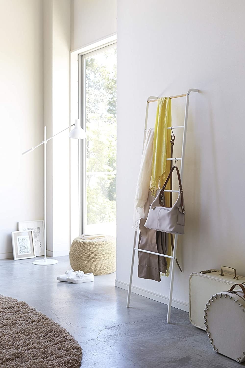 A white leaning ladder against a wall with scarves, pants, and a purse hanging from it 