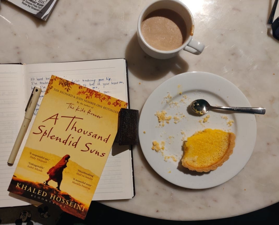 The book placed next to a cup of coffee and a lemon tart.