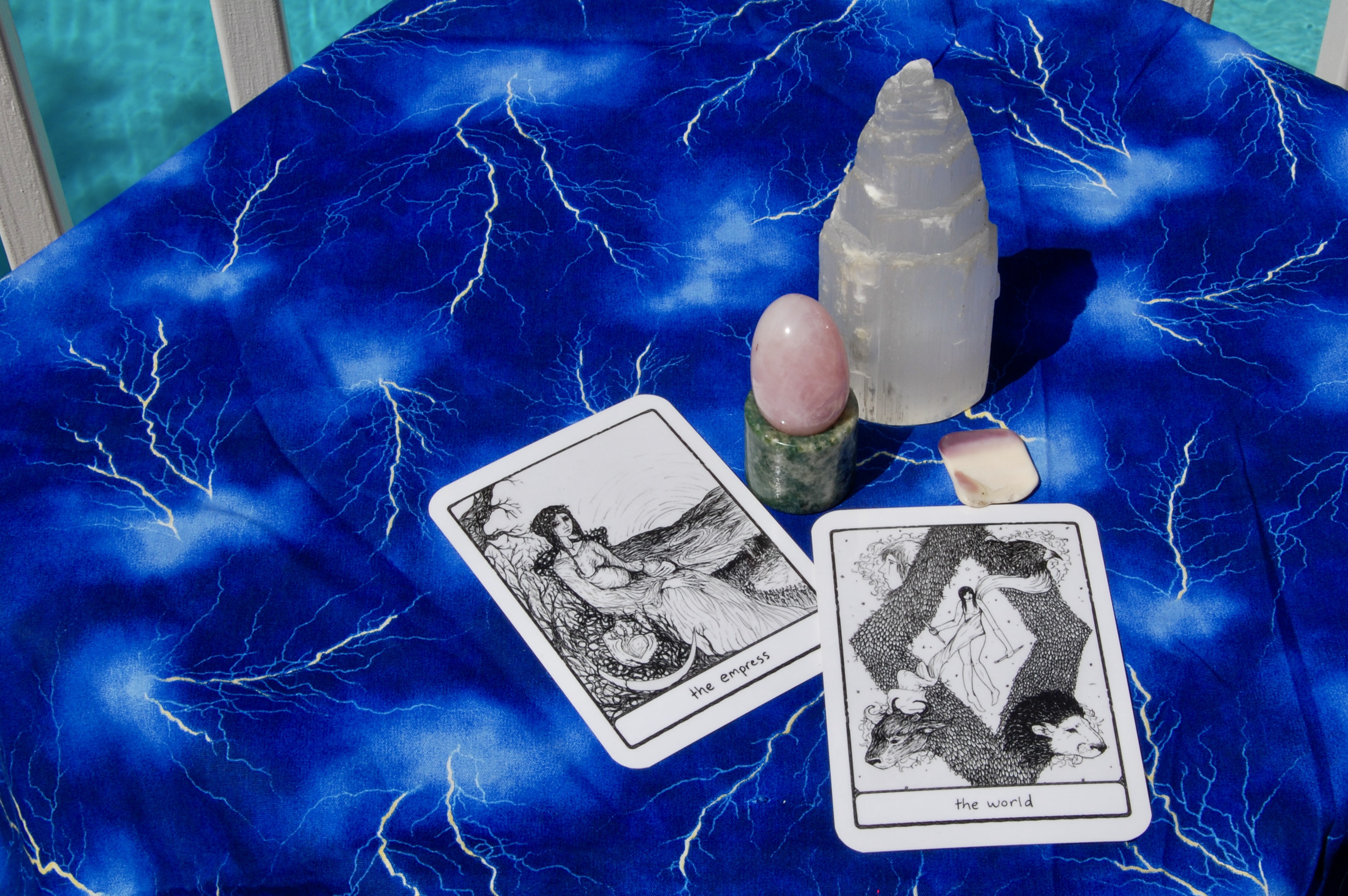 Photo of crystal yoni egg with two tarot cards (Judgement and the High Priestess), plus a selenite tower and a small, square-shaped shell