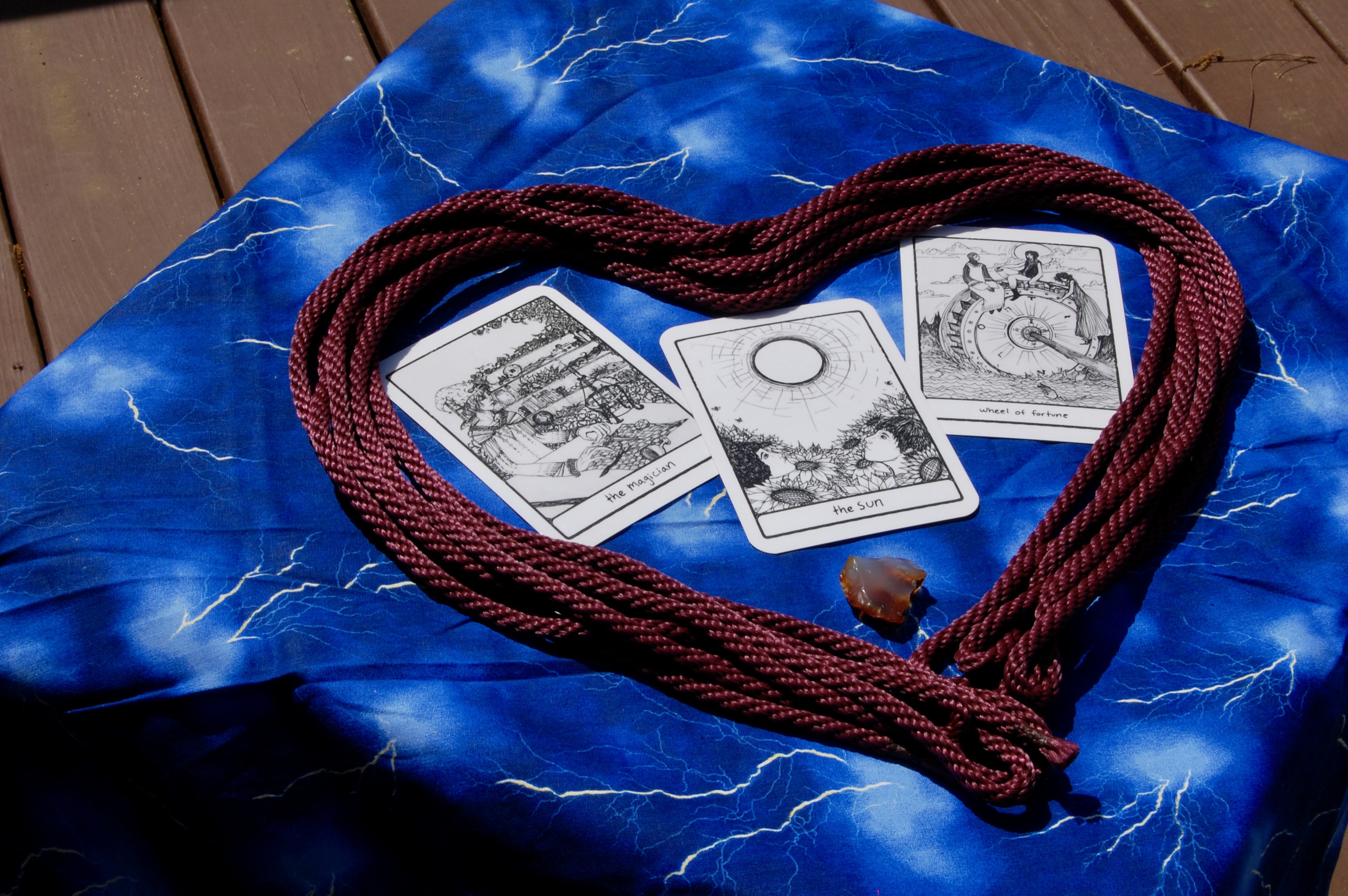 Photo of a rope in a heart shape with three tarot cards (the Magician, the Sun, and Wheel of Fortune), plus a small crystal