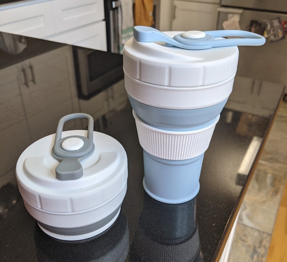 A blue coffee cup with a white thermal sleeve sitting next to a gray version of the cup collapsed down into a small disc 